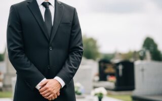 Človek v čiernom obleku stojí na cintoríne pri hrobových kameňoch v tichom pohrebnom prostredí.