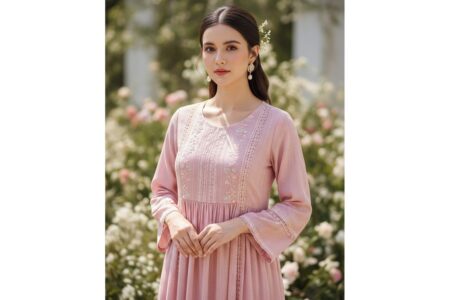 žena v jemných ružových šatách s krajkou stojaca v prírodnom svetle pred rozmazaným kvetinovým pozadím