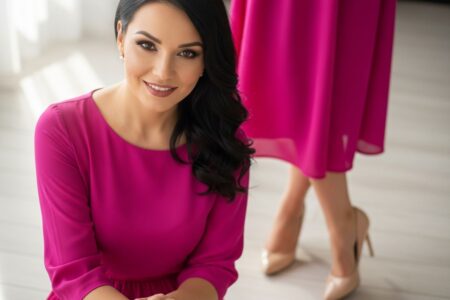 žena v ružových šatách a béžových lodičkách stojaca na svetlej drevenej podlahe